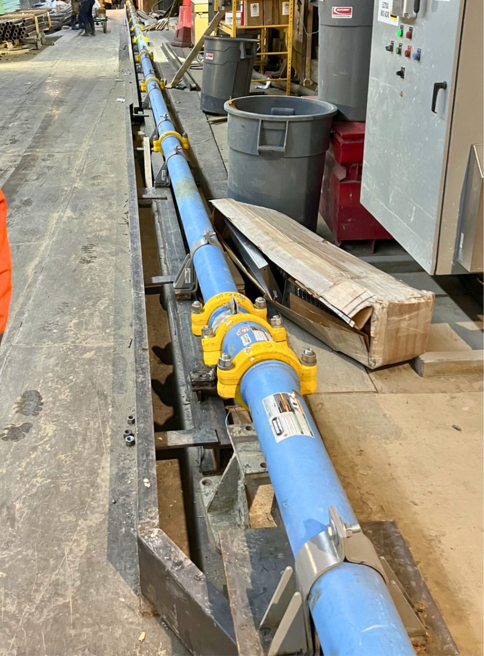 Run of laydown pipe joined with yellow 2-bolt clamps along a bracketed rail